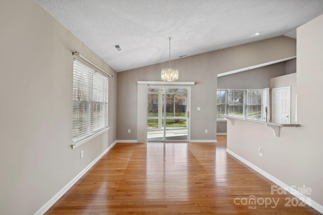 unfurnished dining area with a textured ceiling, an inviting chandelier, light hardwood / wood-style flooring, and vaulted ceiling