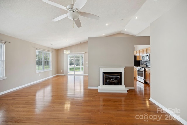 unfurnished living room featuring a textured ceiling, ceiling fan with notable chandelier, lofted ceiling, and hardwood / wood-style flooring