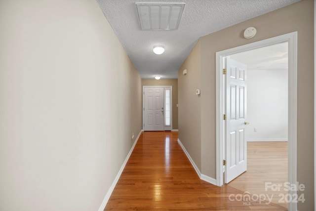 corridor featuring light hardwood / wood-style flooring and a textured ceiling