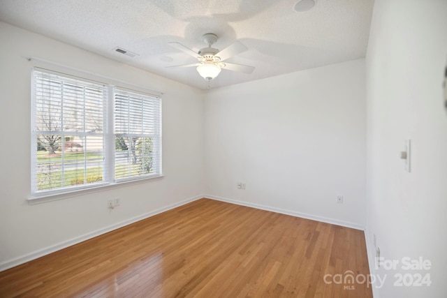 empty room with a textured ceiling, light wood-type flooring, a wealth of natural light, and ceiling fan