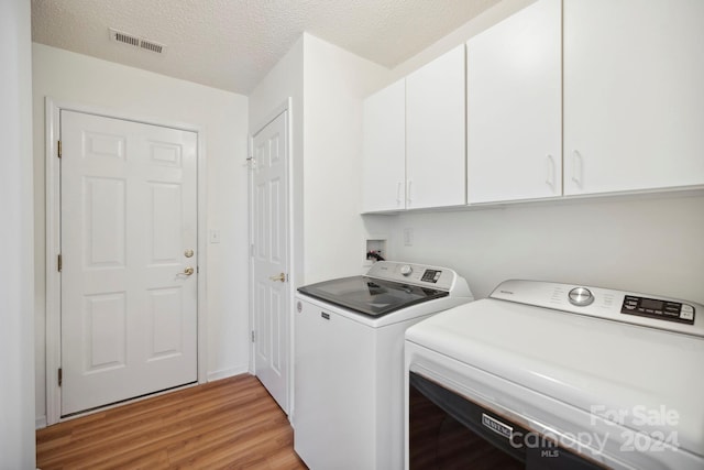 clothes washing area with cabinets, a textured ceiling, light hardwood / wood-style floors, and washing machine and clothes dryer