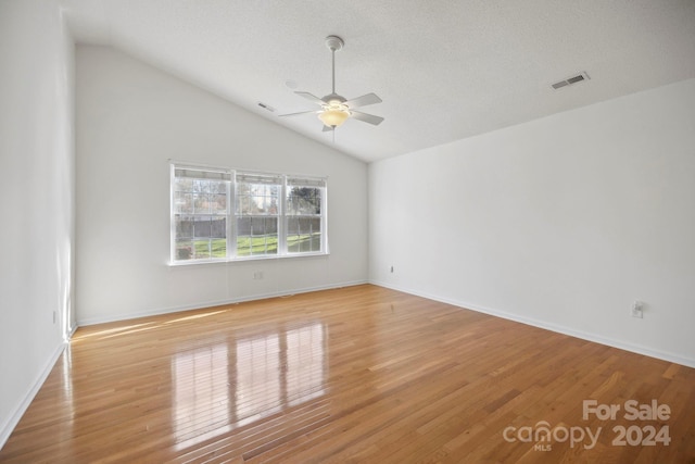 empty room featuring a textured ceiling, light wood-type flooring, vaulted ceiling, and ceiling fan