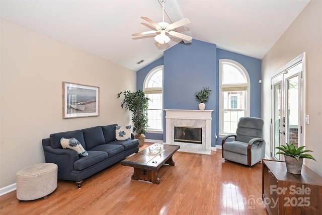 living room with a premium fireplace, a healthy amount of sunlight, vaulted ceiling, and light hardwood / wood-style floors