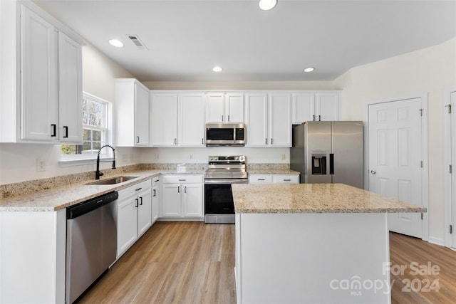 kitchen with sink, light hardwood / wood-style flooring, appliances with stainless steel finishes, a kitchen island, and white cabinetry