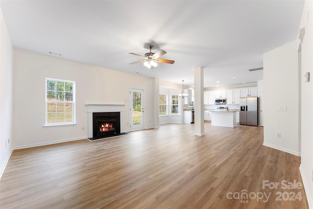 unfurnished living room featuring plenty of natural light, light hardwood / wood-style floors, and ceiling fan with notable chandelier