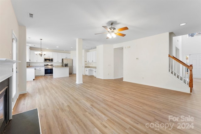 unfurnished living room with ceiling fan with notable chandelier and light hardwood / wood-style floors