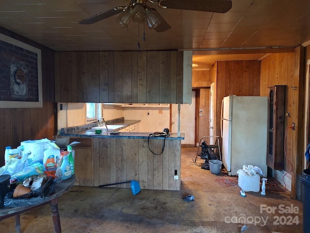 kitchen with kitchen peninsula, concrete flooring, wooden walls, sink, and white fridge