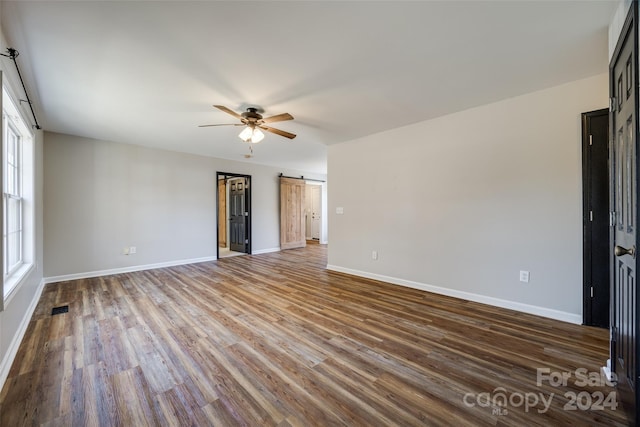 unfurnished room featuring a barn door, hardwood / wood-style flooring, and ceiling fan