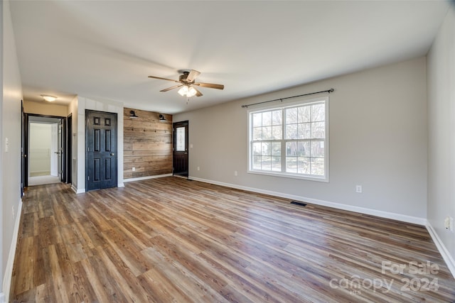 unfurnished bedroom with hardwood / wood-style flooring, ceiling fan, and wooden walls