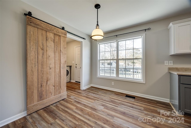 unfurnished dining area with a barn door, washer / clothes dryer, and light hardwood / wood-style flooring