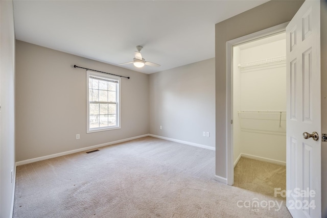 unfurnished bedroom with light carpet, a spacious closet, a closet, and ceiling fan