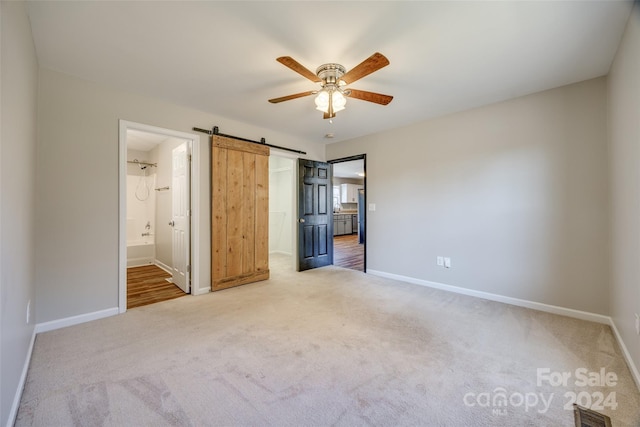 unfurnished bedroom with carpet, a barn door, ensuite bathroom, and ceiling fan