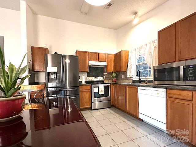 8430 Stoneman Pl, Charlotte, NC 28217 - kitchen featuring under cabinet range hood, stainless steel appliances, tasteful backsplash, brown cabinetry, and dark countertops