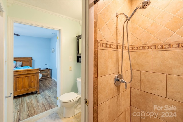 bathroom featuring tiled shower, toilet, hardwood / wood-style floors, and ornamental molding