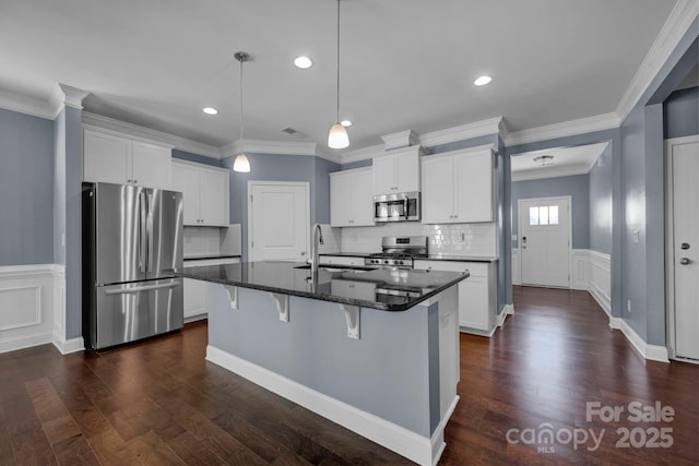 kitchen featuring decorative light fixtures, an island with sink, white cabinets, a kitchen breakfast bar, and stainless steel appliances