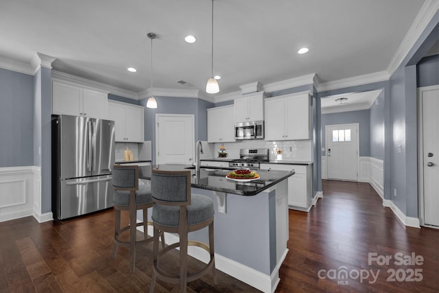 kitchen with white cabinetry, appliances with stainless steel finishes, a center island with sink, and decorative light fixtures