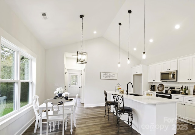 kitchen with a kitchen island with sink, appliances with stainless steel finishes, pendant lighting, white cabinetry, and tasteful backsplash