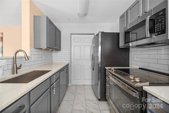 kitchen with backsplash, gray cabinets, sink, and stainless steel appliances