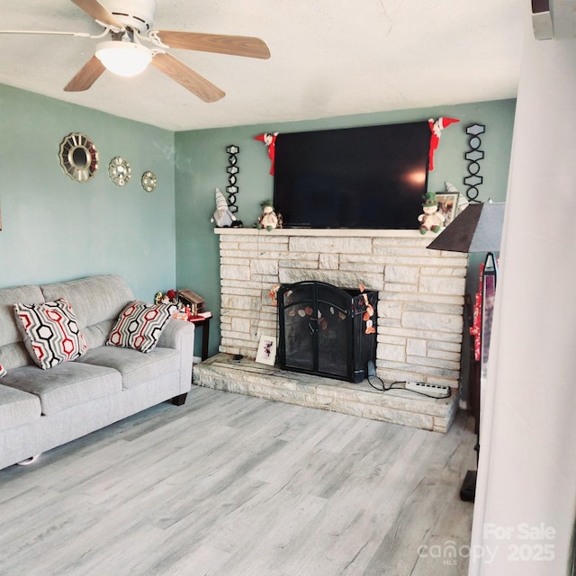 living room featuring a stone fireplace, hardwood / wood-style floors, and ceiling fan