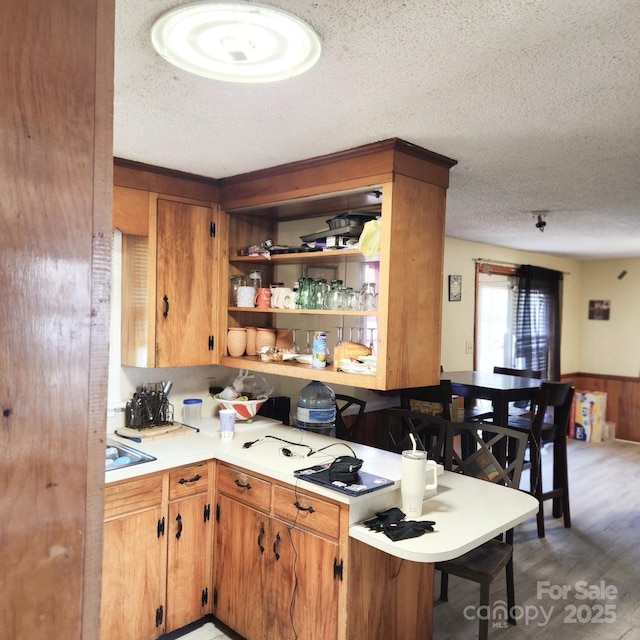 kitchen featuring hardwood / wood-style flooring, a kitchen bar, kitchen peninsula, and a textured ceiling