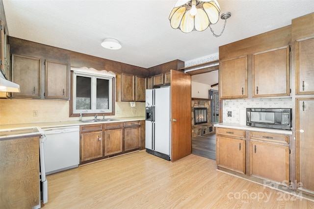 kitchen with white appliances, sink, light wood-type flooring, a textured ceiling, and a fireplace