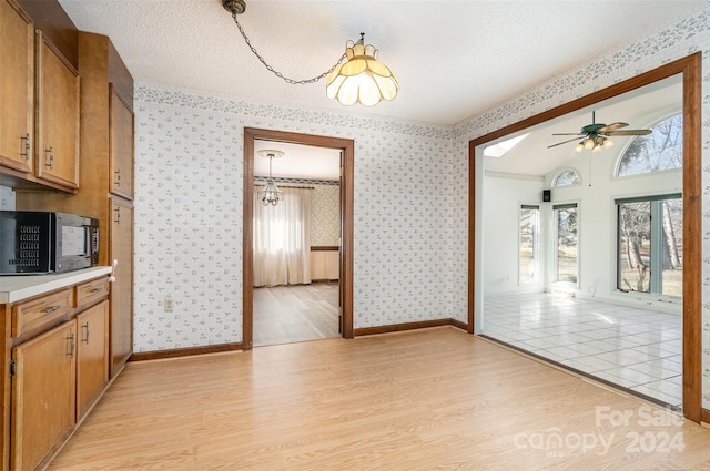 kitchen featuring a textured ceiling, a healthy amount of sunlight, ceiling fan with notable chandelier, and light wood-type flooring