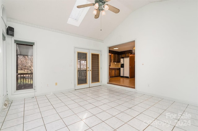 tiled empty room with ceiling fan, vaulted ceiling with skylight, and french doors