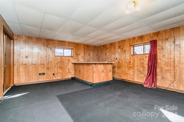 interior space with bar area, a paneled ceiling, and wood walls