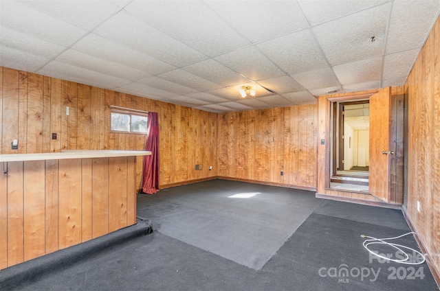 unfurnished room with dark colored carpet, a paneled ceiling, and wooden walls