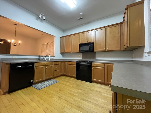 kitchen featuring black appliances, a notable chandelier, light wood-type flooring, pendant lighting, and sink