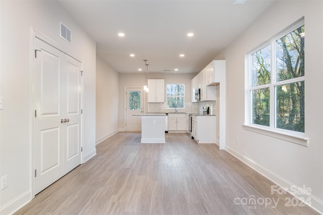 kitchen featuring white cabinetry, backsplash, light hardwood / wood-style floors, pendant lighting, and appliances with stainless steel finishes