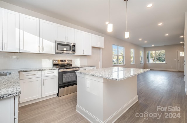 kitchen featuring white cabinets, appliances with stainless steel finishes, light wood-type flooring, and pendant lighting