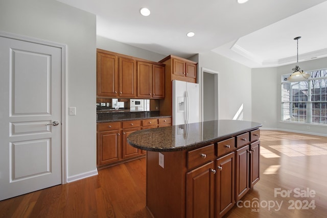 kitchen featuring dark stone counters, wood-type flooring, pendant lighting, a kitchen island, and white fridge with ice dispenser