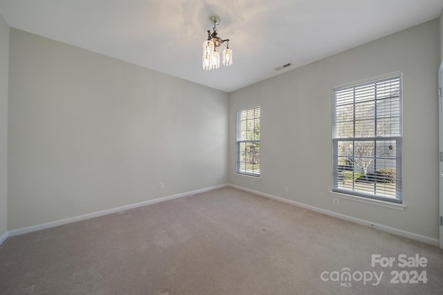 spare room featuring carpet floors and a chandelier