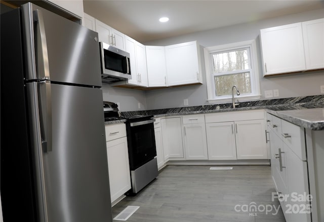 kitchen with appliances with stainless steel finishes, sink, white cabinets, and dark stone counters