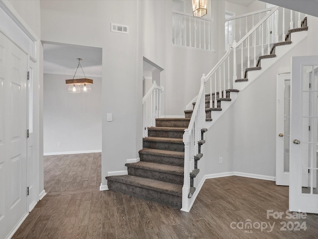 stairway featuring hardwood / wood-style flooring, a towering ceiling, and an inviting chandelier