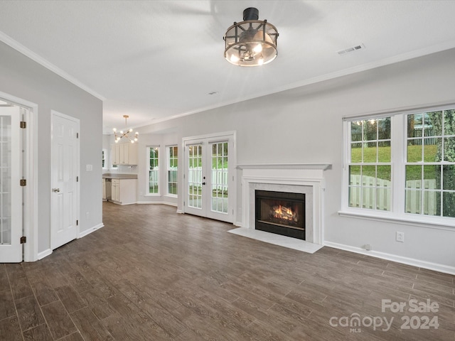 unfurnished living room featuring french doors, a fireplace, crown molding, a chandelier, and dark hardwood / wood-style floors