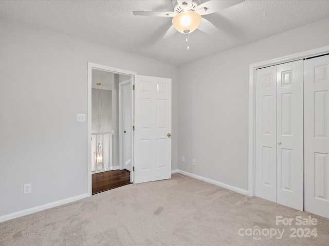 unfurnished bedroom featuring ceiling fan, a closet, light colored carpet, and a textured ceiling