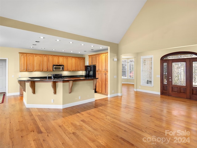 kitchen featuring a kitchen bar, light wood-type flooring, black refrigerator with ice dispenser, high vaulted ceiling, and an island with sink