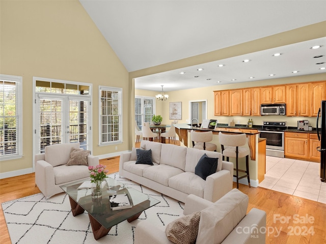 living room featuring high vaulted ceiling, light hardwood / wood-style flooring, and a notable chandelier