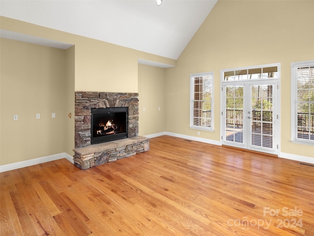 unfurnished living room featuring a fireplace, high vaulted ceiling, french doors, and light wood-type flooring