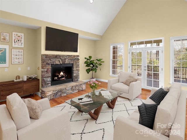 living room featuring light hardwood / wood-style floors, a stone fireplace, and high vaulted ceiling