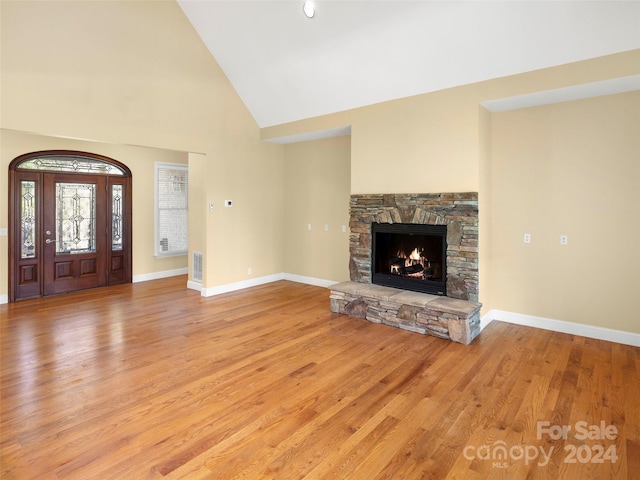 interior space with a stone fireplace, light wood-type flooring, and high vaulted ceiling