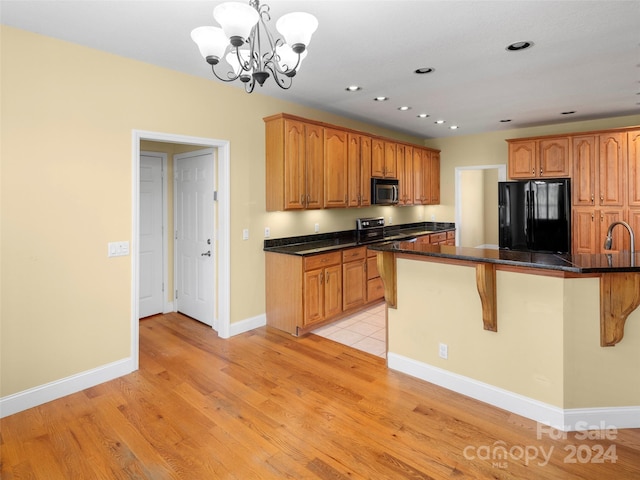 kitchen featuring an inviting chandelier, light hardwood / wood-style flooring, appliances with stainless steel finishes, decorative light fixtures, and a kitchen bar