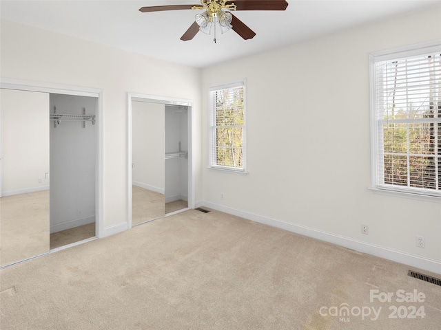 unfurnished bedroom featuring ceiling fan, light colored carpet, multiple closets, and multiple windows