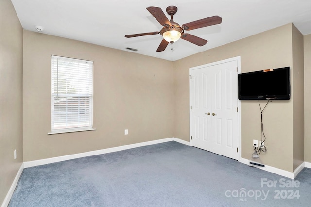 unfurnished bedroom with dark colored carpet, ceiling fan, and a closet