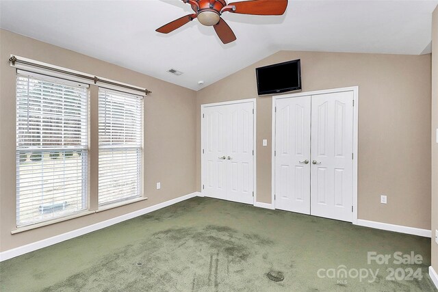 unfurnished bedroom with dark colored carpet, two closets, vaulted ceiling, and ceiling fan