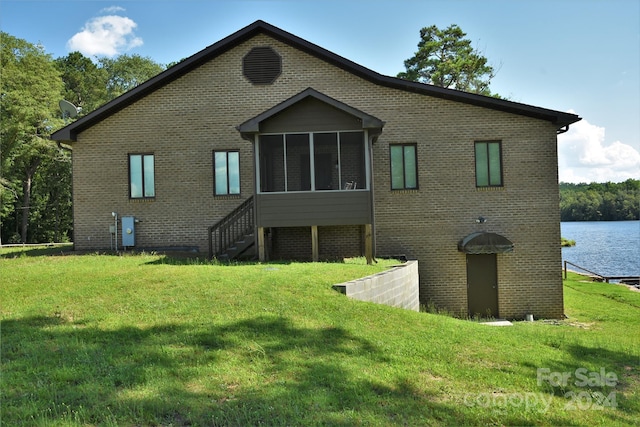 back of house with a sunroom, a water view, and a lawn