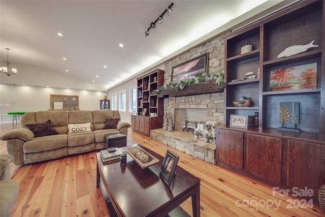 living room featuring built in shelves, a stone fireplace, a notable chandelier, lofted ceiling, and light wood-type flooring