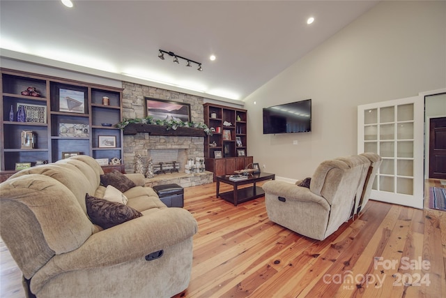 living room featuring rail lighting, light wood-type flooring, lofted ceiling, and a fireplace